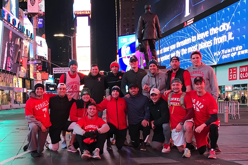 Sixteen lacrosse alumni wearing Cornell gear with Times Square in the background