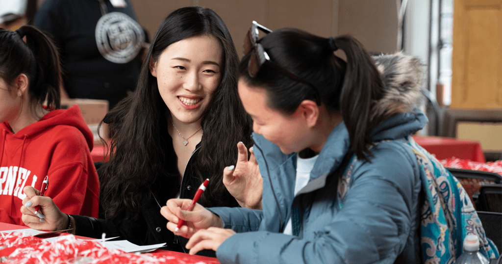 Cornell students talking and smiling as they write thank-you postcards