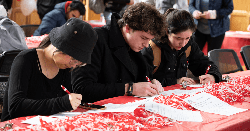 A row of students write thank-you postcards at Willard Straight Hall